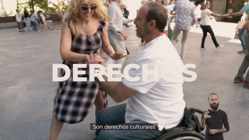 Una mujer y un hombre en silla de ruedas bailando en una plaza son Derechos Culturales.